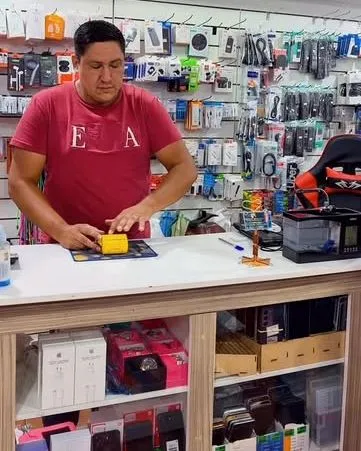 Balcão da loja com a parede de capinhas, fones e carregadores ao fundo